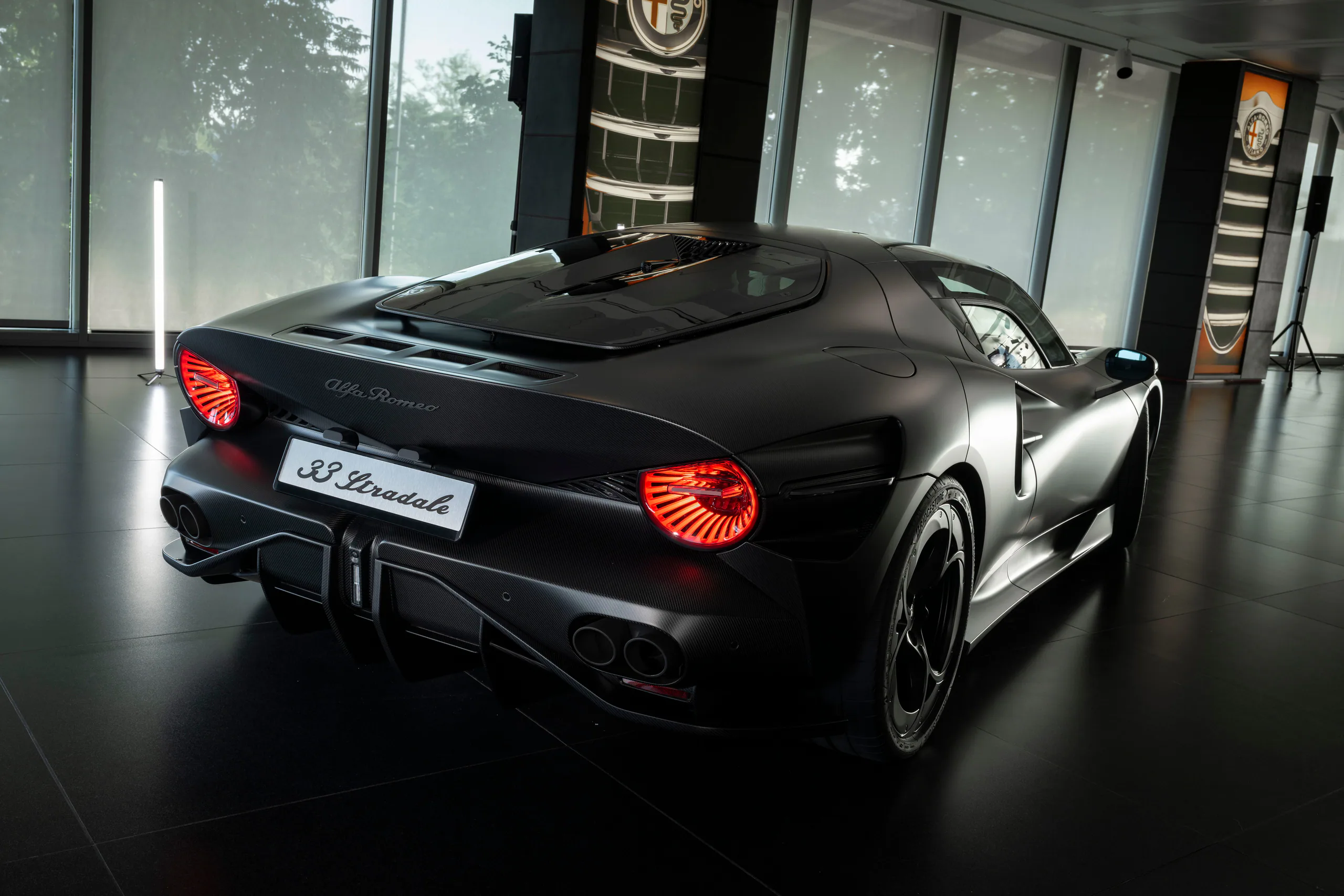 Black Alfa Romeo 33 Stradale sports car showcased indoors with distinctive rear lighting and sleek aerodynamic design.