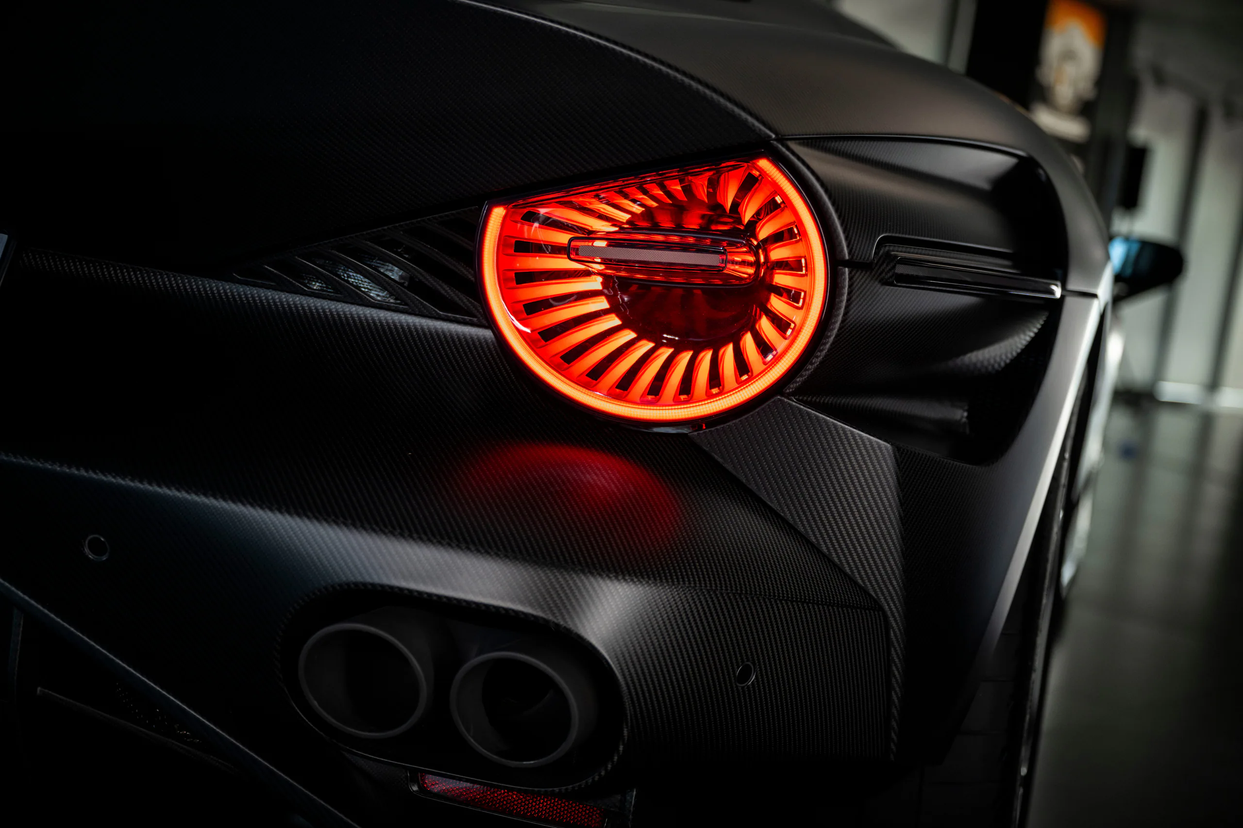 Close-up of a car's rear light with a sleek design and glowing red accents on a carbon fiber surface.