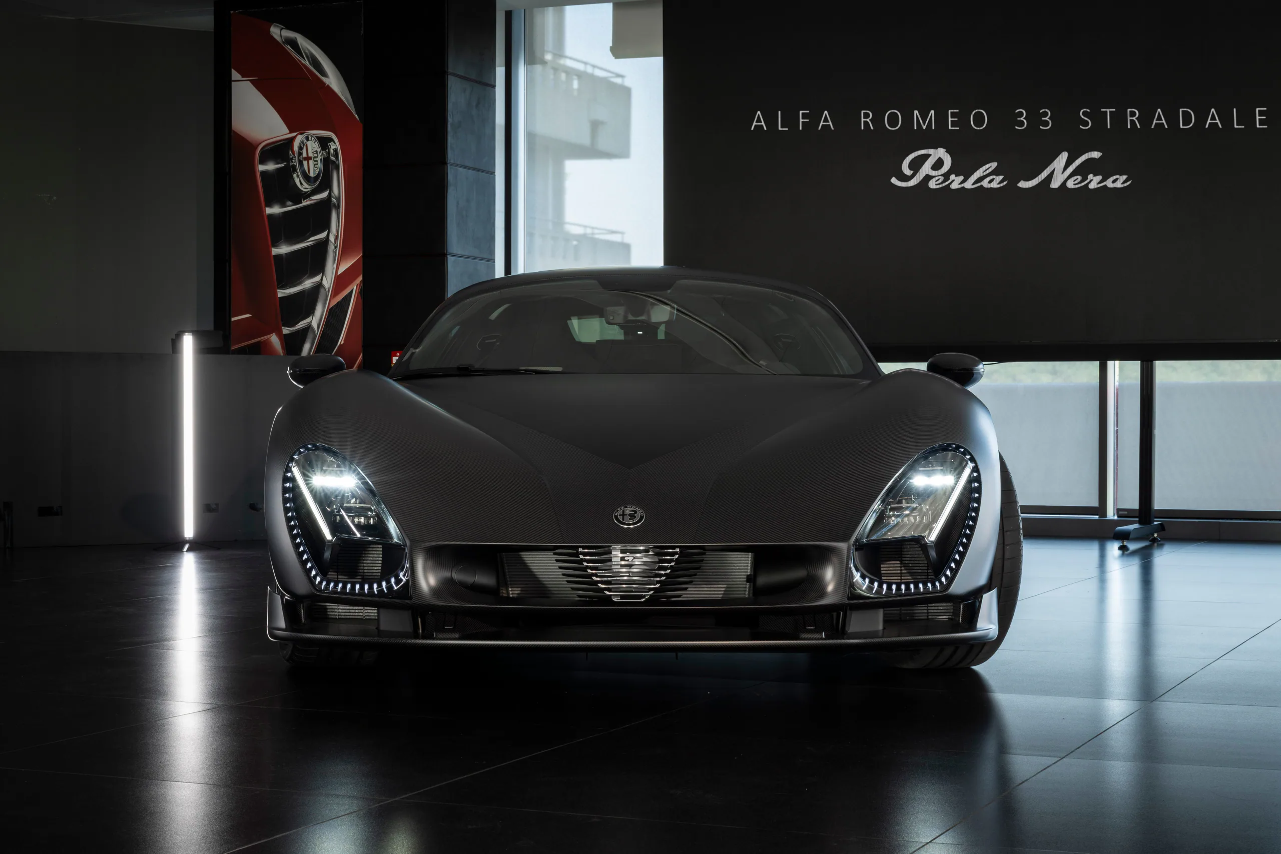 Alfa Romeo 33 Stradale in a showroom, featuring a sleek black design and distinctive headlights.
