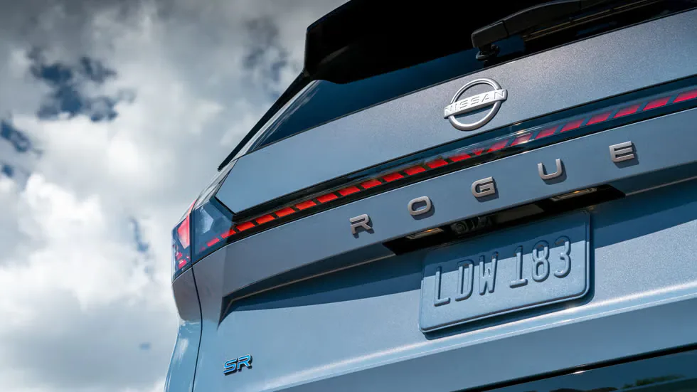 Rear view of a Nissan Rogue with the model name and license plate visible against a cloudy sky.