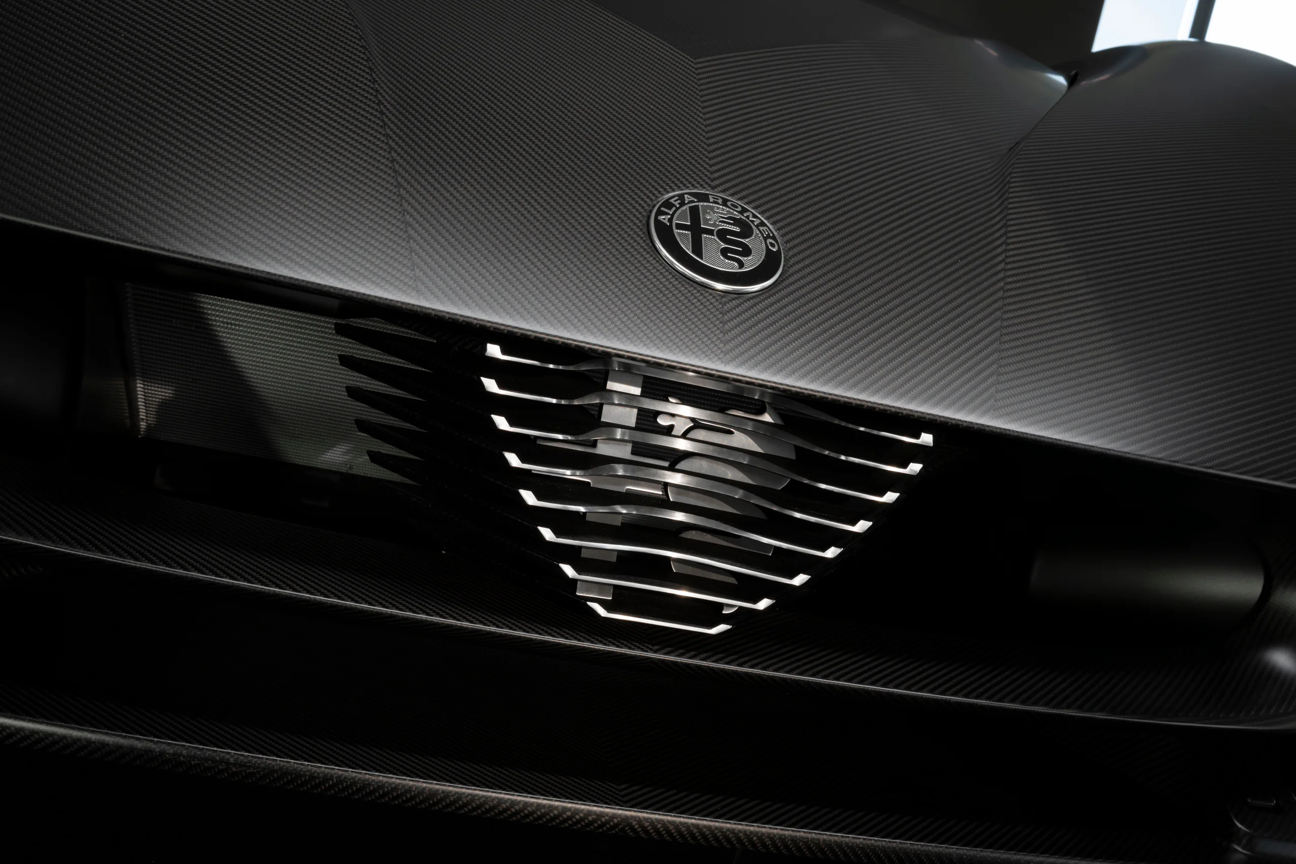 Close-up of a car grille featuring sleek carbon fiber design and the Alfa Romeo emblem.