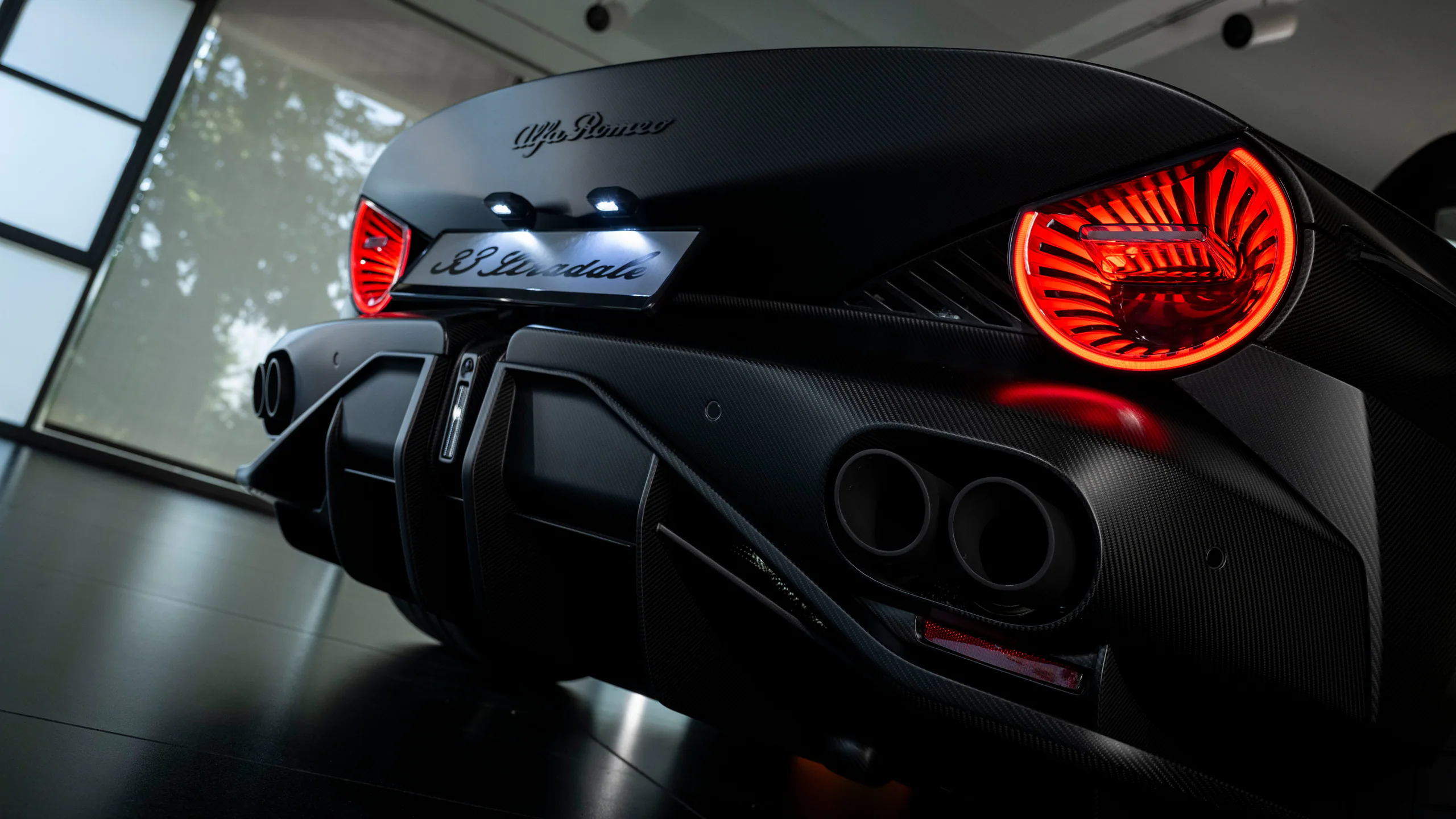 Rear view of a sleek black Alfa Romeo sports car showcasing its distinctive taillights and carbon fiber details.